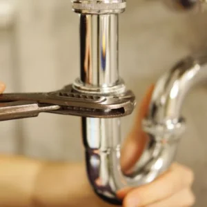 Plumber tightening a chrome sink trap with a wrench
